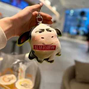 Close-up of funny cow plush keychain with unique meme expression and red text