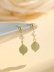 Detailed close-up of elegant gold dangle earrings with green jade beads and white pearls