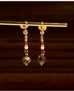 Detalle de pendientes colgantes de cuarzo ahumado y granate con clips de oro