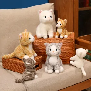 Peluche di gatti realistici in vari colori e pose esposti sopra un cesto di vimini intrecciato
