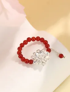 Primer plano de un anillo de cuentas de ágata roja con un delicado colgante de flor de plata.