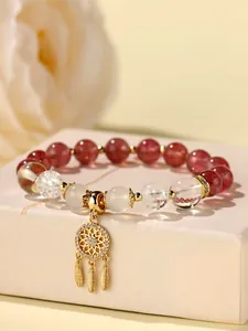 Makroaufnahme eines Perlenarmbandes mit klaren Kristallen und goldenem Traumfänger.