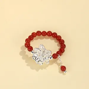 Vista detallada de un anillo de cuentas de ágata roja con un elegante dije de flor de plata.