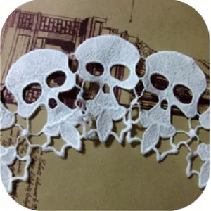 Detalle de encaje blanco soluble en agua con bordado de calaveras y hojas decorativas.