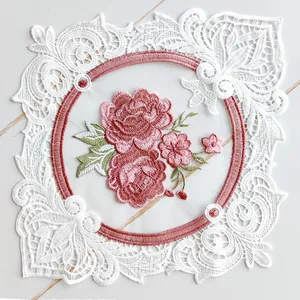 Detail of pink floral embroidery and white lace border on a square decorative coaster