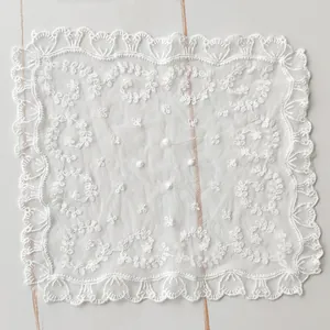 Detailed view of a square white lace mesh doily with intricate floral embroidery