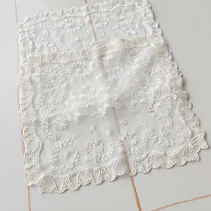 Detailed macro view of white floral lace embroidery on a minimalist square tablecloth.