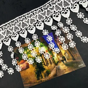 Detail of white water-soluble milk silk lace fringe with heart and floral tassel