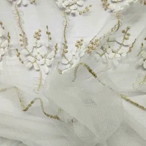 Primo piano di ricamo floreale bianco e oro su tessuto di pizzo a rete