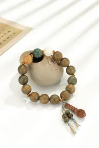Vue détaillée d'un bracelet en bois de santal vert avec pompons ethniques et perles sculptées.