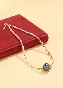 Nahaufnahme einer eleganten Halskette mit Lackperlen und weißen Kristallen auf rotem Buch.