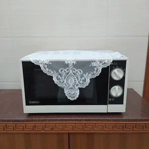 Close-up view of a white lace embroidered cover with elegant floral patterns on a microwave