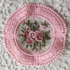 Detalle macro de posavasos redondo de encaje rosa con bordado floral de rosas estilo vintage