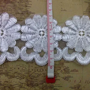 Primer plano del encaje bordado plateado con motivos florales y cinta métrica de referencia
