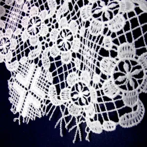 Close-up detail of white water-soluble lace fabric with hollow embroidered floral pattern