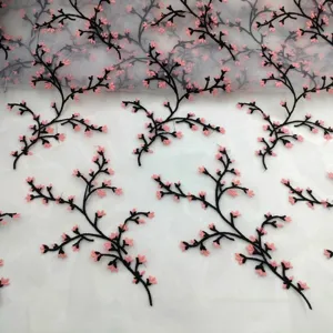 Detail of pink cherry blossom embroidery on white organza lace fabric with black stems