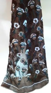 Detailed view of colorful floral embroidery on dark brown sheer organza fabric mesh.