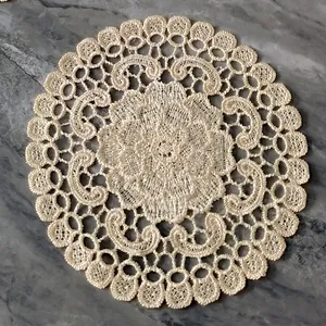 Detailed macro view of cream round floral lace embroidered doily coaster on gray marble