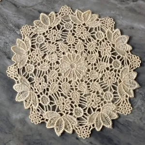 Detail view of vintage cream lace embroidered circular coaster on grey marble surface