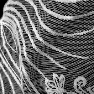 Macro detail showing white polyester embroidered lace pattern on fine mesh fabric
