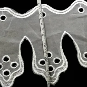 Close-up of white water-soluble lace trim with scalloped eyelet embroidery and measurement tape.