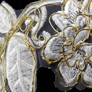 Macro detail of white and gold corded lace trim with intricate floral patterns.