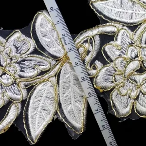 Detailed macro shot of white and gold cord embroidered floral lace trim on black organza fabric