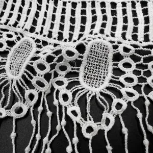 Detailed close-up of white cotton lace crochet fabric with intricate hollow patterns and fringe.