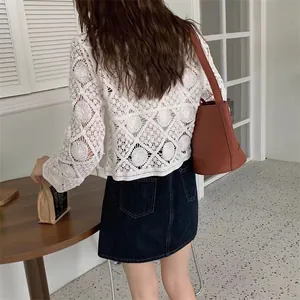 Back view of a white lace crochet long sleeve cardigan styled with a denim skirt