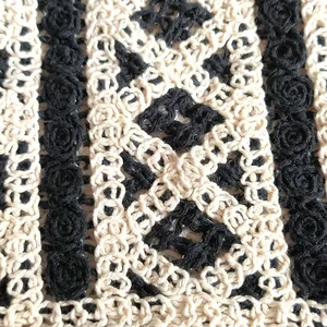 Close-up of delicate hollow crochet knit pattern with black rose embroidery detail.