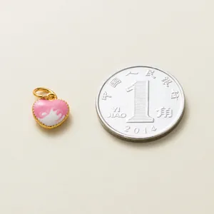 Gros plan d'un pendentif en forme de cœur en émail rose et blanc avec une pièce de monnaie