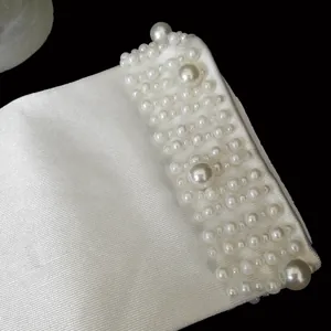 Close-up of white bridal glove cuff featuring elegant pearl beadwork on satin fabric.