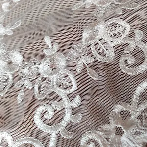 Detailed macro view of intricate white floral embroidery on premium mesh lace fabric