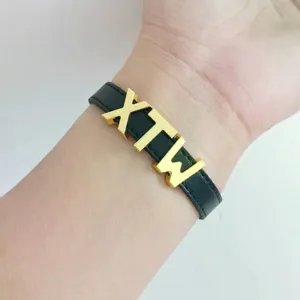 Primo piano di perline con lettere in lega dorata da 10 mm 'XTW' su un cinturino in pelle nera