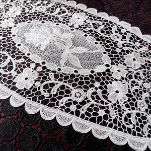 Detailaufnahme einer feinen weißen Spitze mit Blumenstickerei auf einem Tischset.