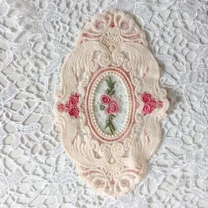 Detail der rosa Rosenstickerei auf einem eleganten ovalen Spitzenuntersetzer im Vintage-Stil