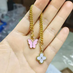 Close-up detail of a gold chain with pink butterfly and white letter X enamel charms