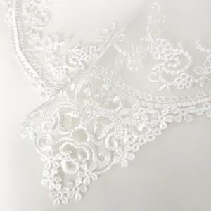 Detailed macro view showing delicate white floral lace embroidery on sheer mesh fabric