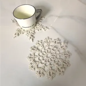 Detail view of two white crochet snowflake coasters on marble surface with a mug.