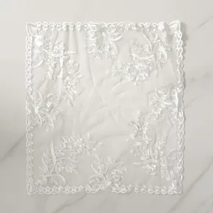 Detailed view of white lace embroidered placemat with floral patterns on mesh fabric