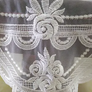 Dettaglio di una tovaglia a rete bianca con ricami floreali intricati.