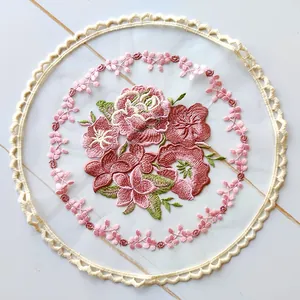 Detailed view of colorful floral embroidery on white mesh coaster with scalloped lace edge