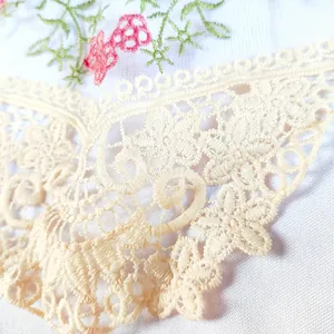 Gros plan détaillé montrant les motifs floraux complexes sur dentelle brodée crème.