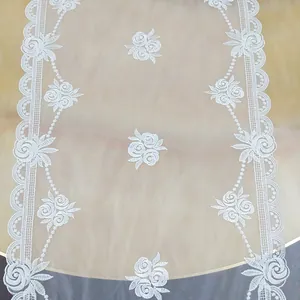 Primo piano di runner da tavola in pizzo bianco con eleganti rose ricamate e base in rete.
