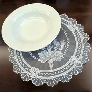 Detailed macro view of white embroidered lace placemat with floral pattern under a bowl