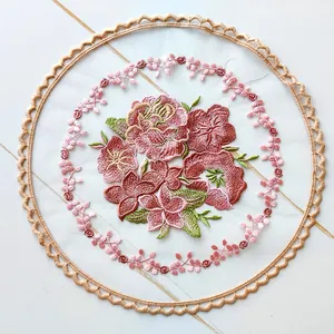 Detailed view of floral embroidery on a circular mesh coaster with scalloped lace border