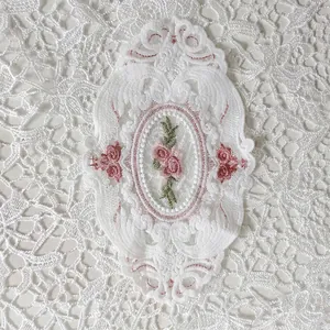 Exquisites Detail der Stickerei mit rosa Rosen auf einem weißen ovalen Spitzenuntersetzer