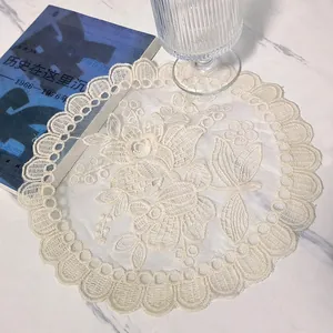 Close-up of beige circular lace placemat with delicate floral embroidery on marble surface.