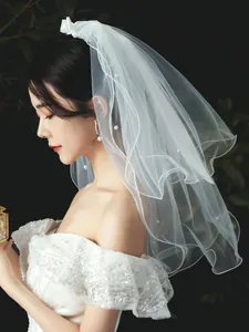 Detail view of short white bridal veil with pearl accents and bow headband.
