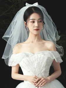 Detailed view of elegant short white bridal veil with bow and pearl accents on model